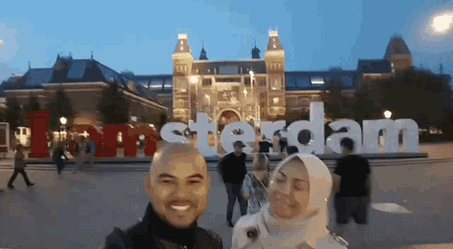 a man and a woman are posing in front of a sign that says amsterdam