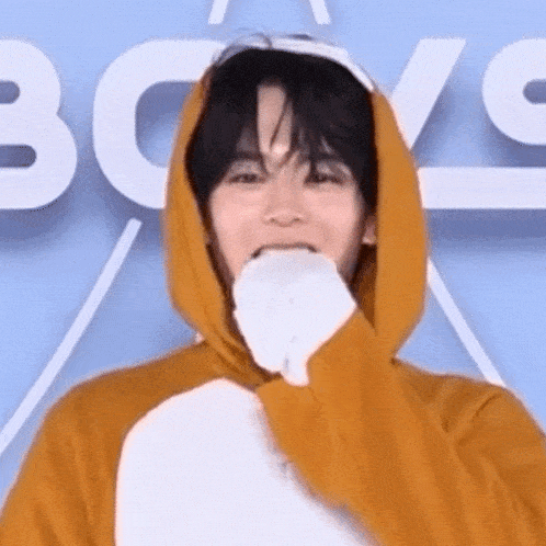 a young man wearing a yellow hoodie and a white glove is covering his mouth .