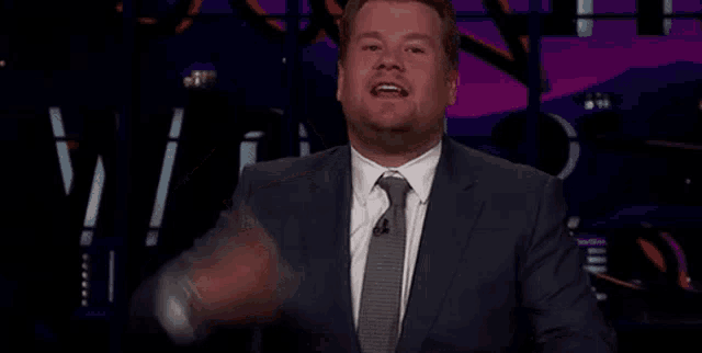 a man in a suit and tie is making a funny face while sitting on a stage .