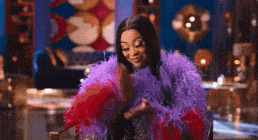 a woman in a purple and red feathered coat is holding a fan in her hand .