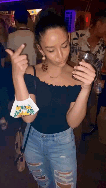 a woman wearing a black off the shoulder top and ripped jeans is holding a glass