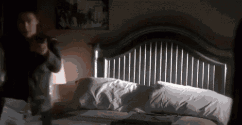 a person is standing in front of a bed with a gun in their hand