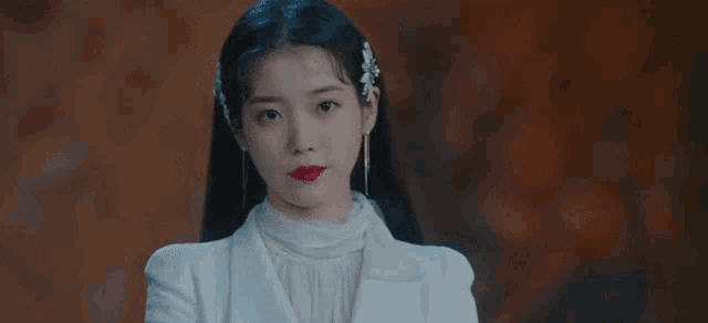 a woman wearing a white jacket and red lipstick is standing in front of a wall .