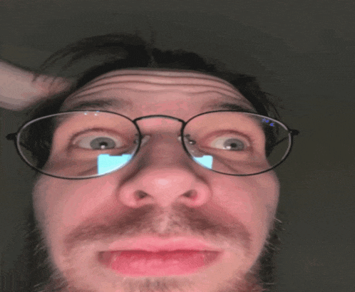 a close up of a man 's face with glasses and a beard making a funny face