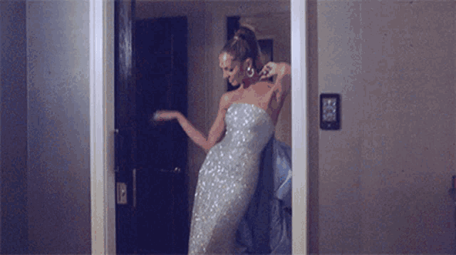 a woman in a silver dress is standing in front of a mirror in a room .