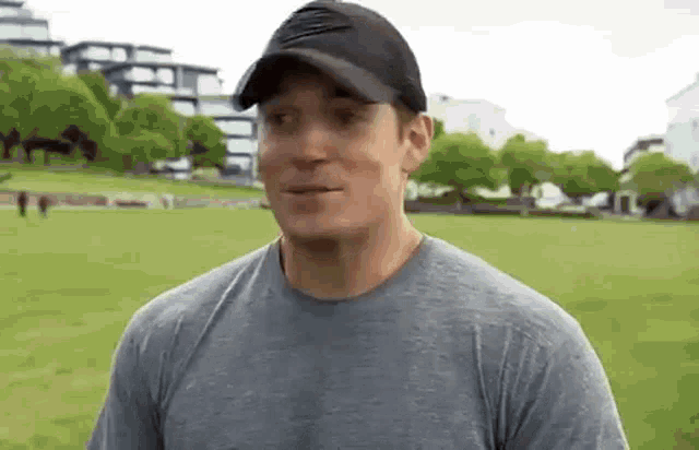 a man wearing a hat and a t-shirt is standing in a park .