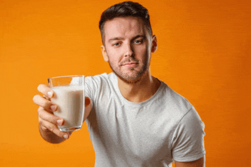 a man holding a glass of milk in front of an orange background