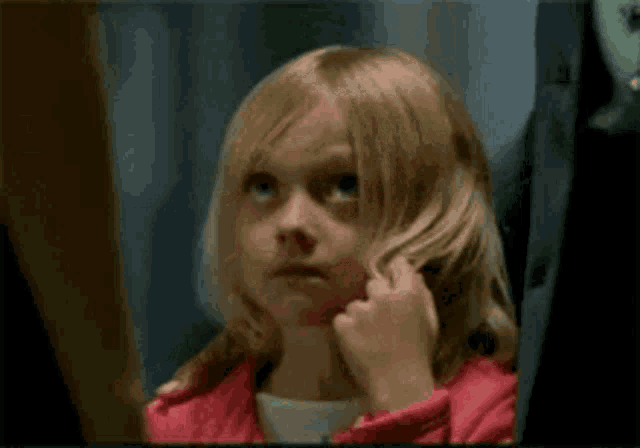 a little girl in a pink jacket is looking at her hair in the mirror