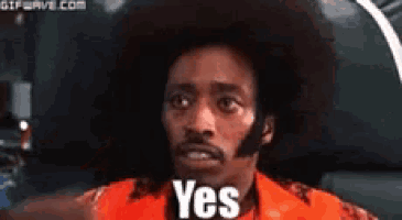 a man with an afro is sitting in a car with the word yes on his chest .