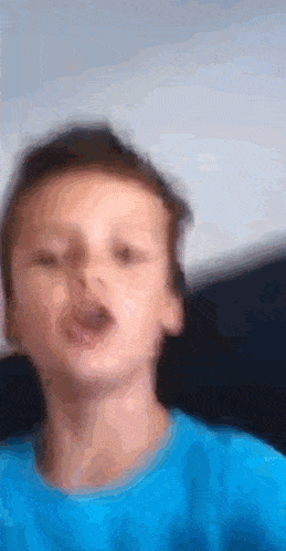 a young boy wearing a blue shirt is making a funny face
