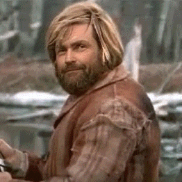 a man with long blonde hair and a beard is wearing a brown jacket and looking at the camera .