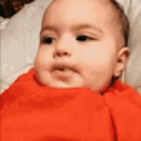a baby wearing a red sweater is sitting on a bed .