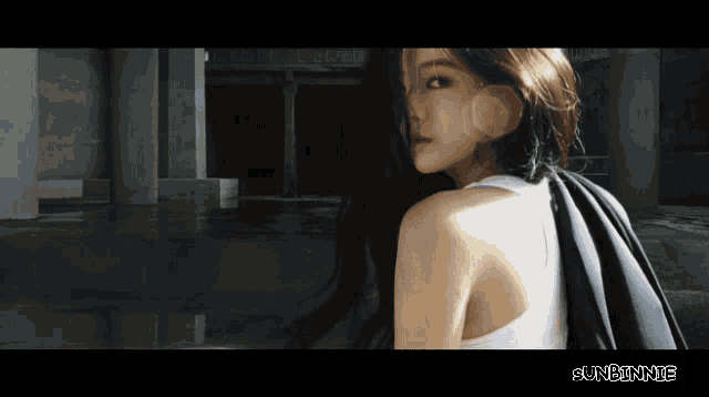 a woman in a white tank top stands in a dark room with the words sunbinnie below her