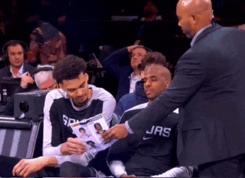 a man in a suit talks to a man in a spurs shirt