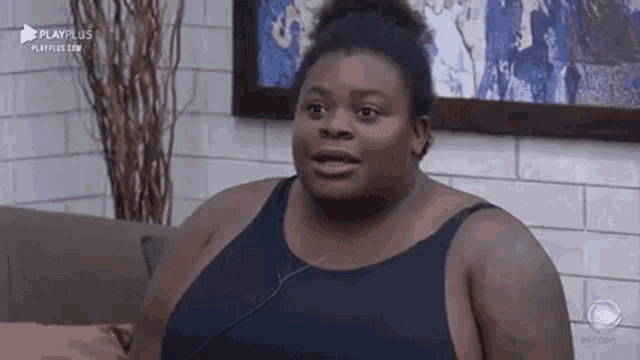 a very fat woman is sitting on a couch wearing a black tank top and headphones .