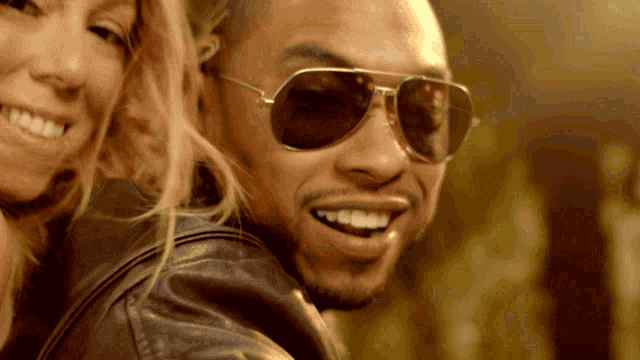 a man wearing sunglasses and a leather jacket smiles with a woman