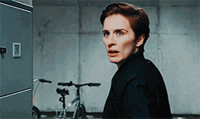 a woman in a black shirt is standing in a room with a bicycle in the background