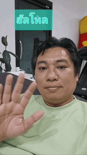 a man in a green shirt holds up his hand in front of a sign that says ' sal '