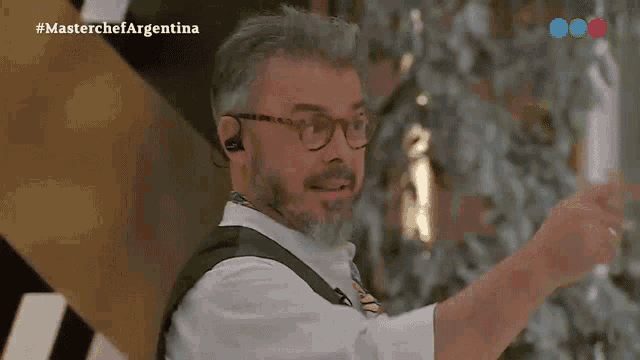 a man with glasses and a beard is wearing ear buds and a vest .