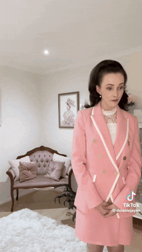 a woman in a pink suit is standing in front of a couch .