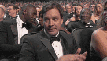 a man in a tuxedo is sitting in a crowd of people clapping .
