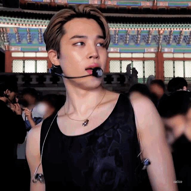 a young man wearing a black tank top and a microphone looks at the camera