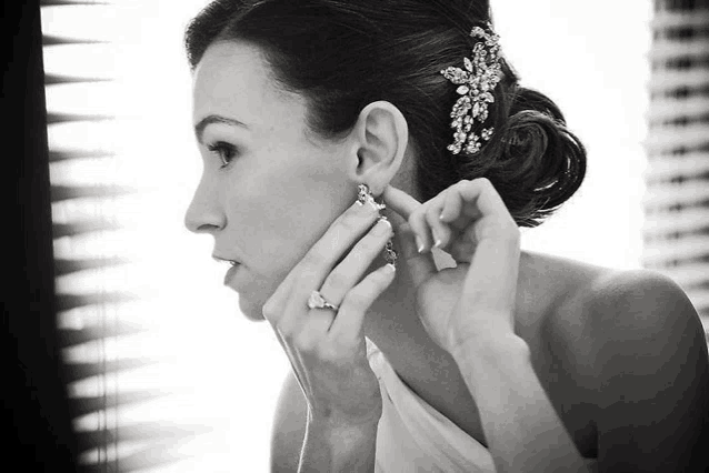 a woman adjusts her earrings in front of a mirror