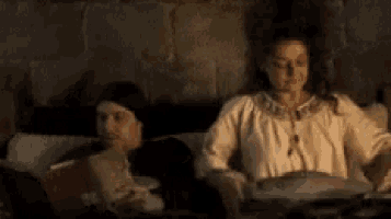a woman is sitting on a couch reading a book while a man sits next to her .