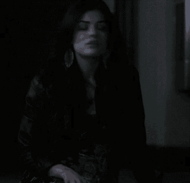 a woman wearing a black jacket and earrings is sitting in a dark room
