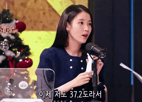 a woman stands in front of a microphone with a sign that says merry christmas on it