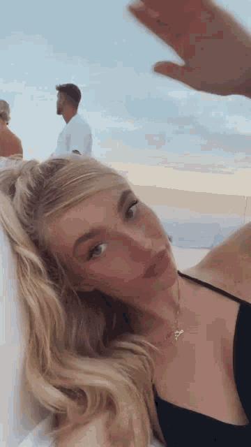 a woman in a black dress is laying on a beach with a man standing behind her .