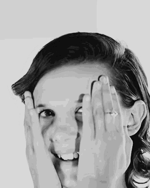a young girl is covering her eyes with her hands and smiling .