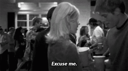 a black and white photo of a woman saying `` excuse me '' in a crowded room .