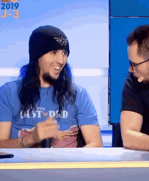 a man wearing a blue shirt that says best dad is talking to another man