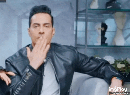 a man in a leather jacket is blowing a kiss while sitting on a couch ..