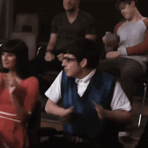 a man in a blue vest is sitting in the audience clapping