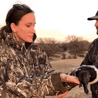 a woman in a camo jacket holds a duck in her hand