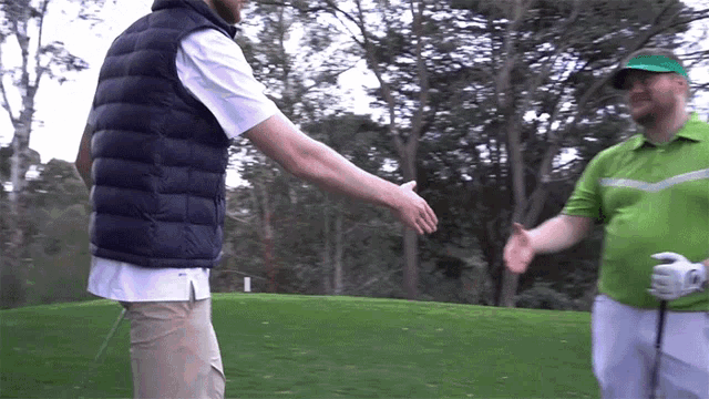 two men shaking hands on a golf course with one wearing a green shirt
