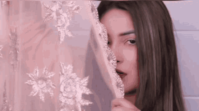 a woman is peeking through a pink curtain with her eyes closed .