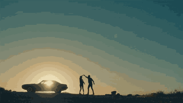 a man and a woman dancing in front of a car at sunset