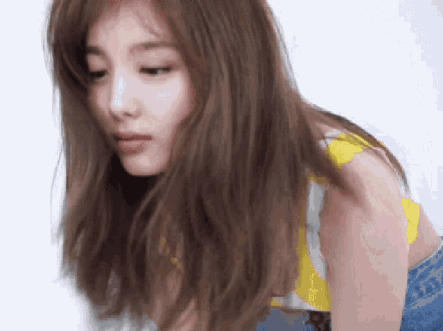 a woman with long brown hair is wearing a yellow top and jeans