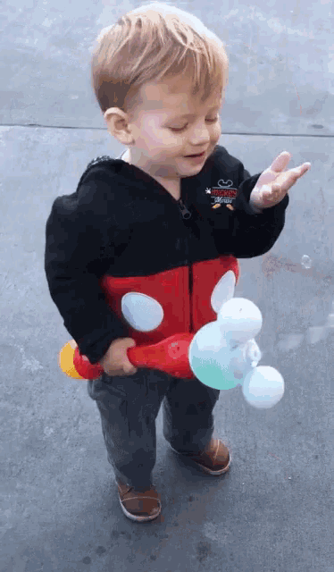 a little boy wearing a mickey mouse jacket is holding a soap bubble maker