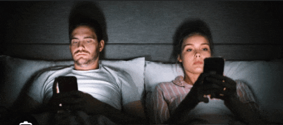 a man and woman are laying in bed looking at their phones