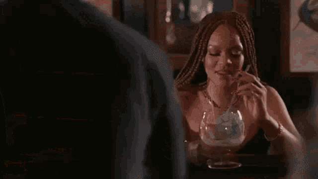 a woman is sitting at a bar drinking a cocktail from a glass .