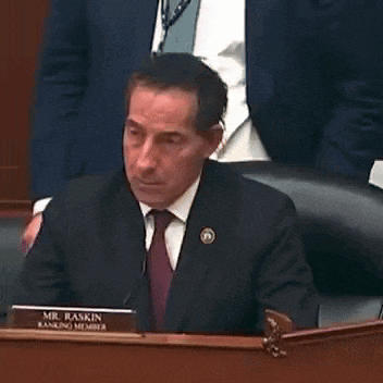 a man in a suit and tie is sitting at a desk with a name plate that says mr. baskin .