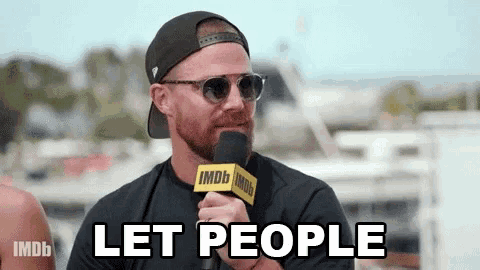 a man in a hat and sunglasses is holding a microphone and saying let people .