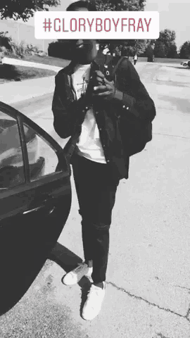 a black and white photo of a man standing next to a car with #gloryboyfray