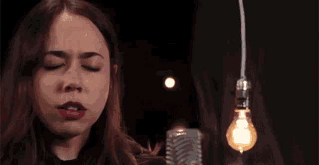 a woman is singing into a microphone in front of a light bulb hanging from the ceiling .