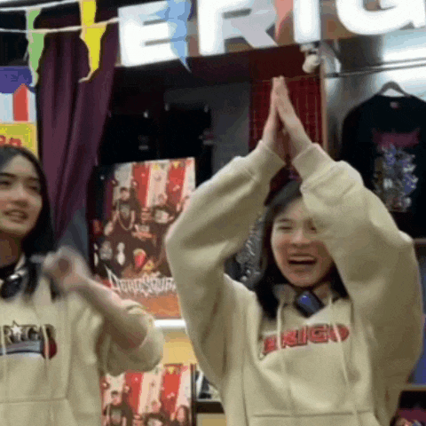 two women are giving each other a high five while wearing hoodies .