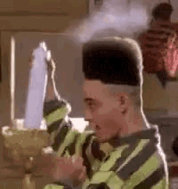 a man with a very high top hairstyle is holding a bottle of hair spray .